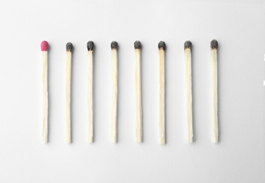 Row of burnt matches and whole one on white background, top view. Uniqueness concept
