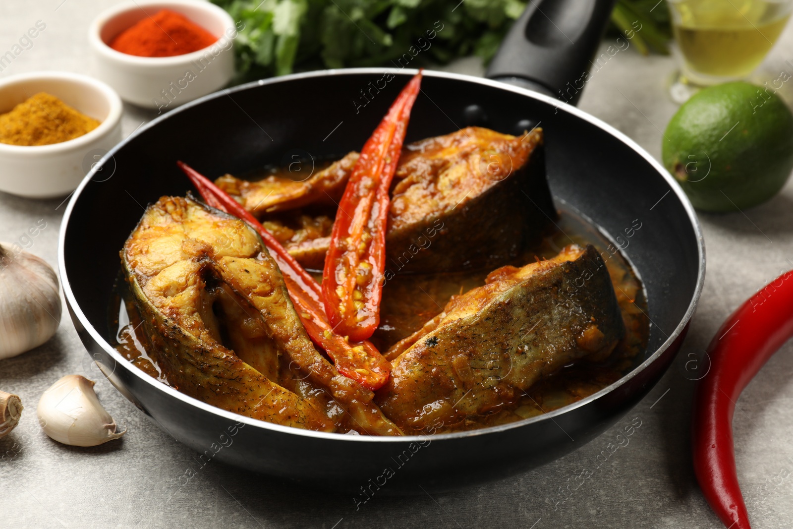 Photo of Tasty fish curry in frying pan and ingredients on light grey table, closeup. Indian cuisine