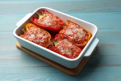 Photo of Tasty stuffed peppers in dish on light blue wooden table