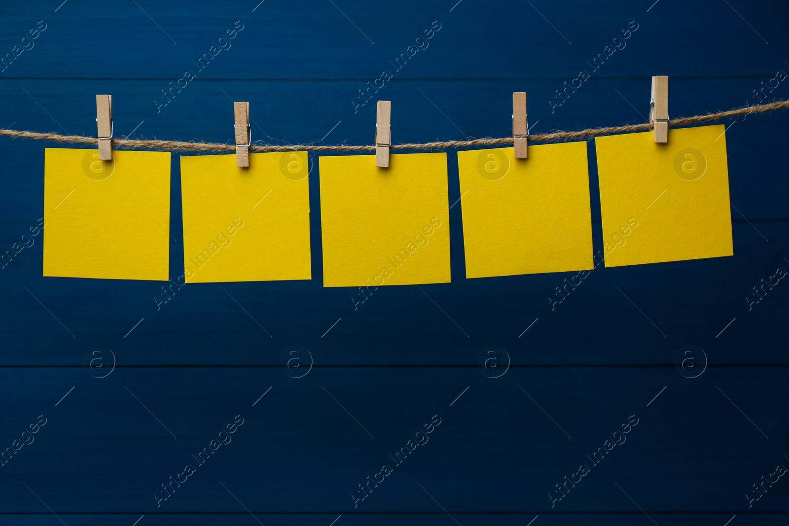 Photo of Clothespins with blank notepapers on twine against blue wooden background. Space for text