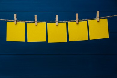 Photo of Clothespins with blank notepapers on twine against blue wooden background. Space for text