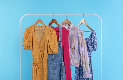 Photo of Rack with stylish women`s clothes on wooden hangers against light blue background