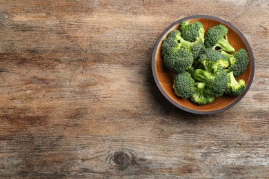 Photo of Wooden bowl of fresh broccoli on table, top view with space for text