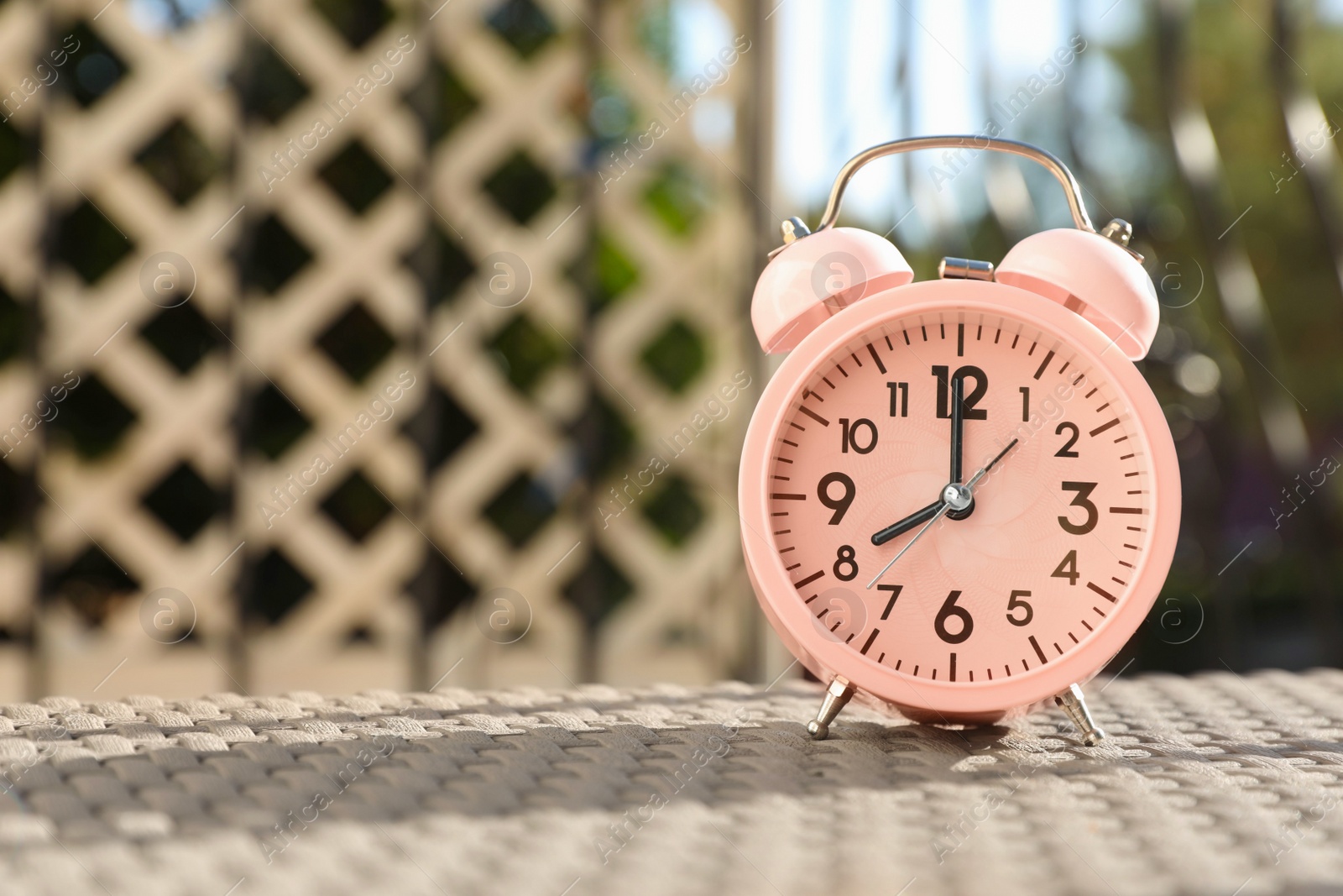 Photo of Pink alarm clock on table outdoors at sunny morning. Space for text