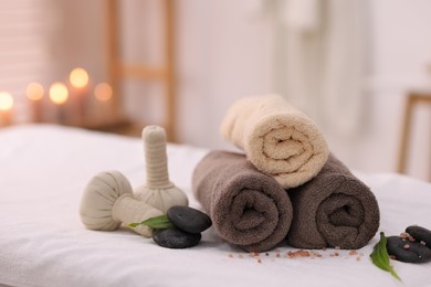 Photo of Spa stones, rolled towels and herbal bags on massage table indoors