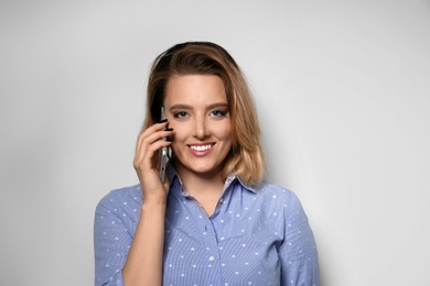 Portrait of beautiful young woman talking on phone against light background