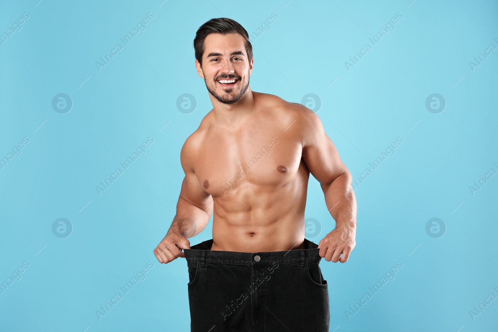 Photo of Young man with slim body in old big size jeans on light blue background