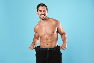 Photo of Young man with slim body in old big size jeans on light blue background