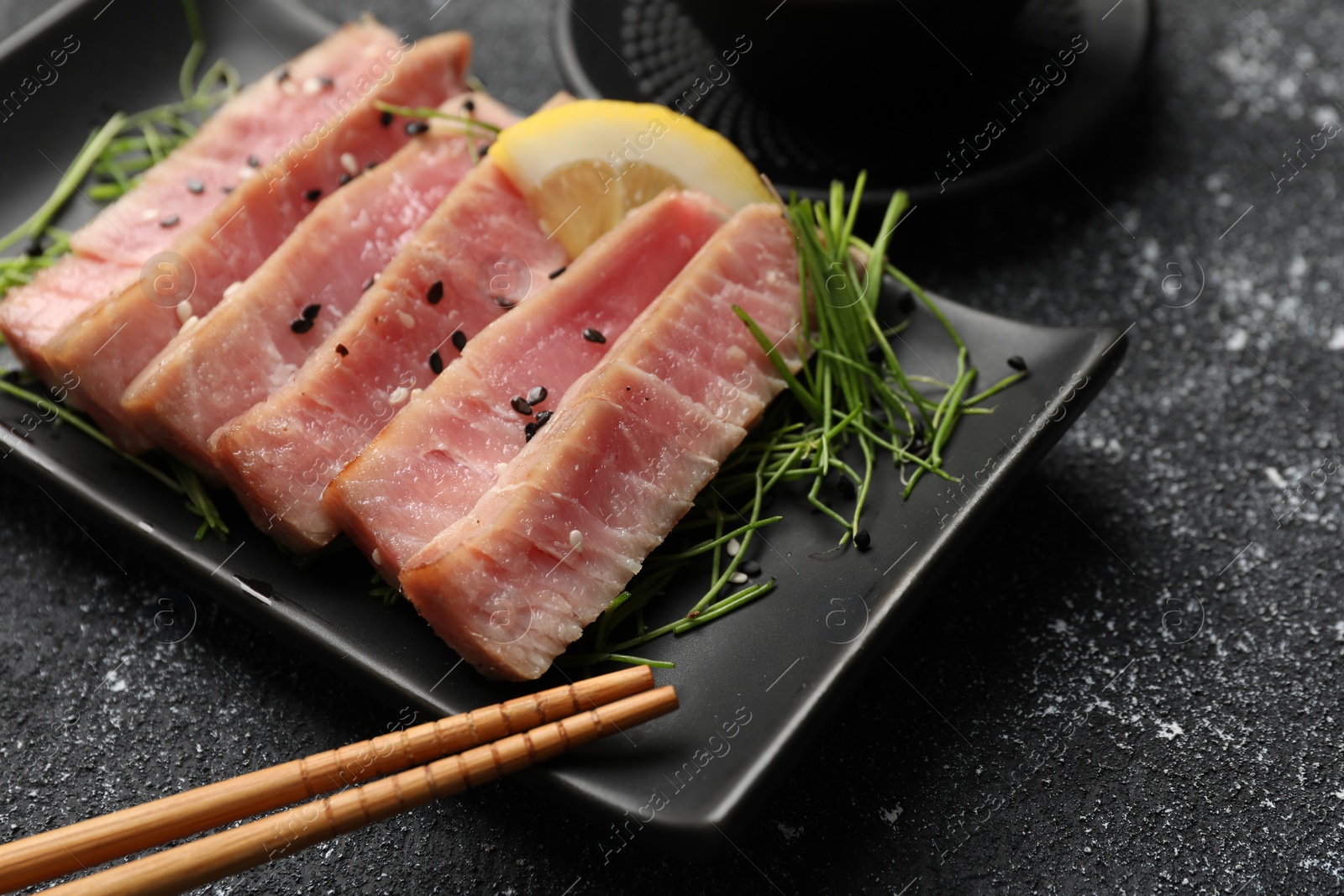 Photo of Pieces of delicious tuna steak served on black table, closeup