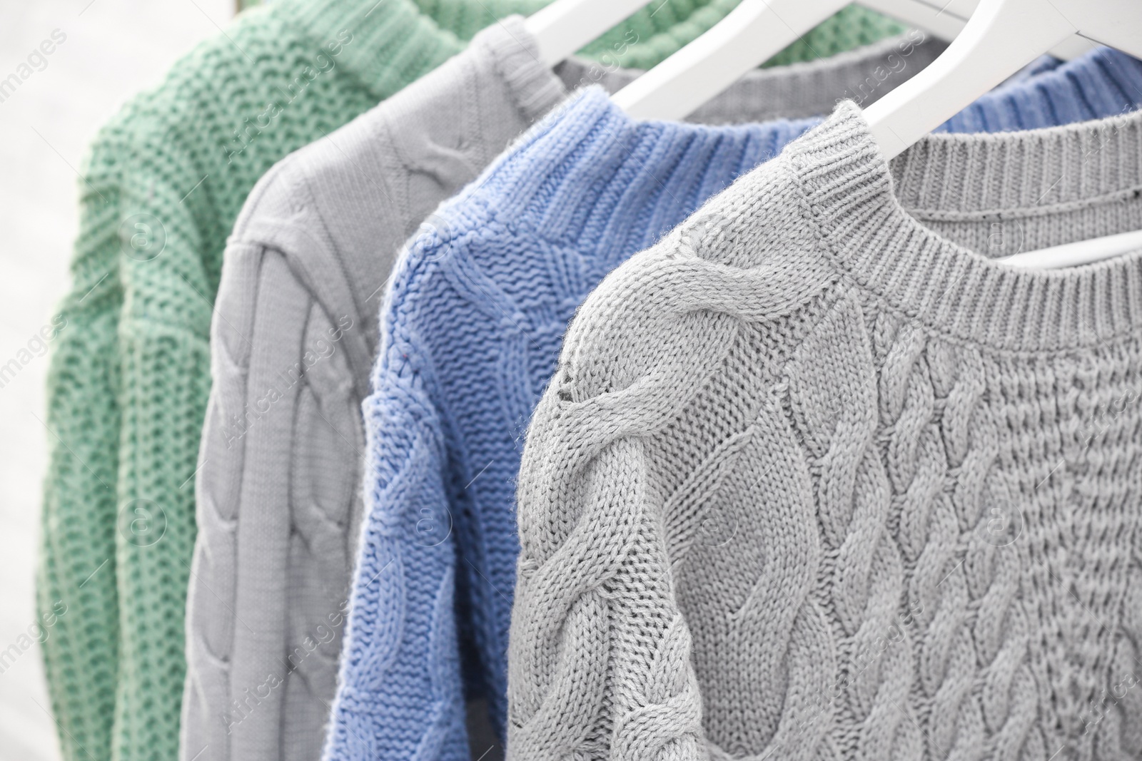 Photo of Collection of warm sweaters hanging on rack, closeup