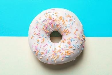 Delicious glazed doughnut with sprinkles on color background, top view