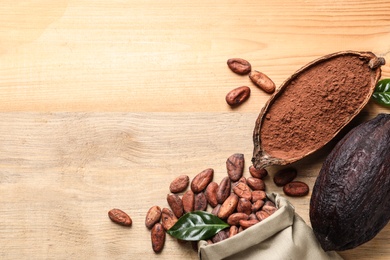 Flat lay composition with cocoa pods and bag of beans on wooden table, space for text