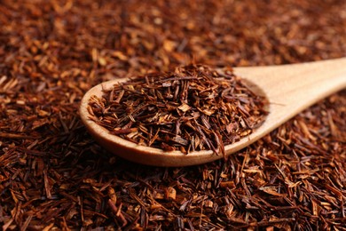 Photo of Heap of dry rooibos tea leaves with wooden spoon, closeup view