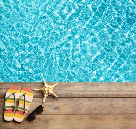 Image of Beach accessories on wooden deck near swimming pool, flat lay. Space for text 