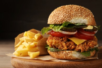 Delicious burger with crispy chicken patty and french fries on wooden table, closeup