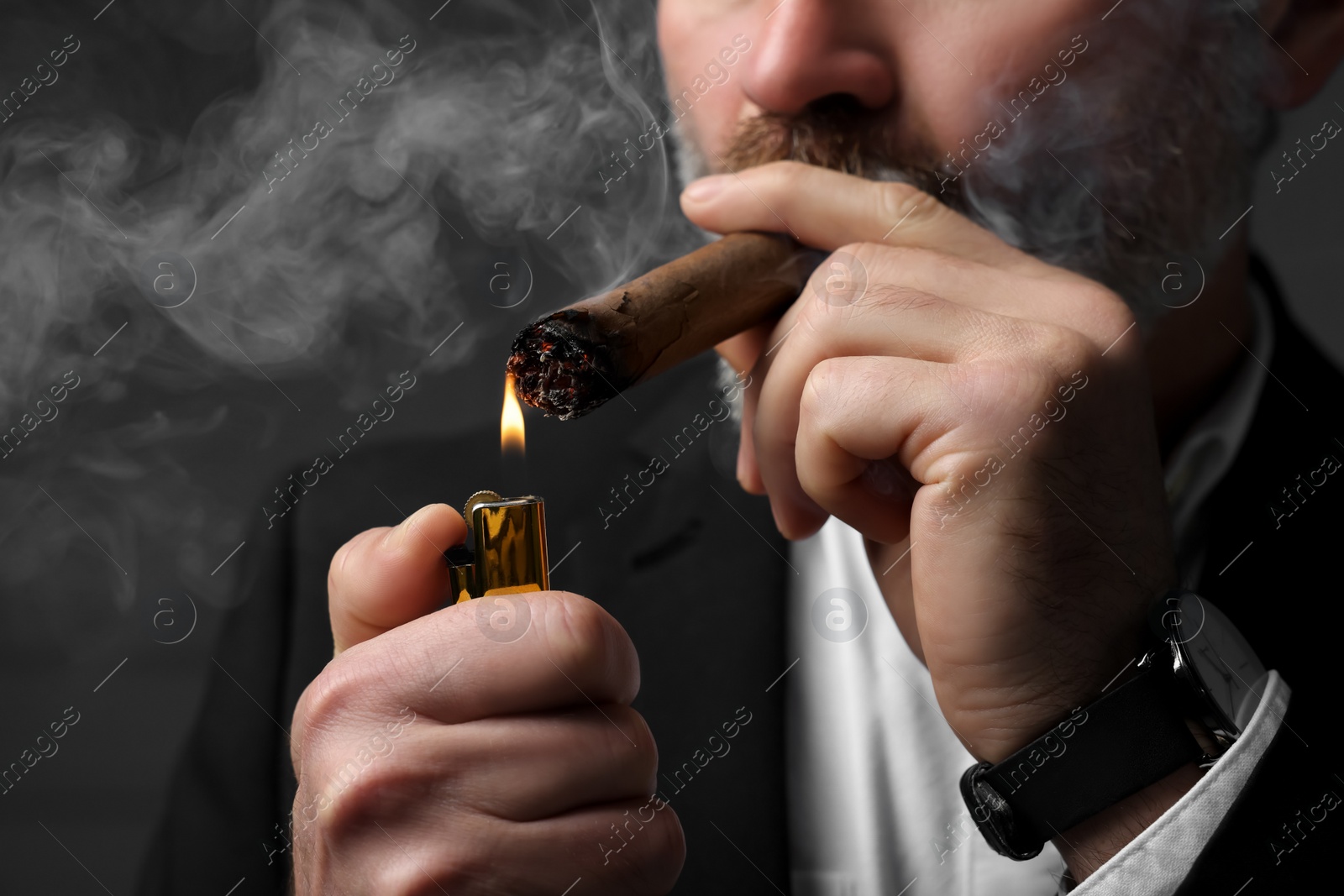 Photo of Bearded man lighting cigar on dark grey background, closeup