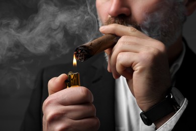 Photo of Bearded man lighting cigar on dark grey background, closeup