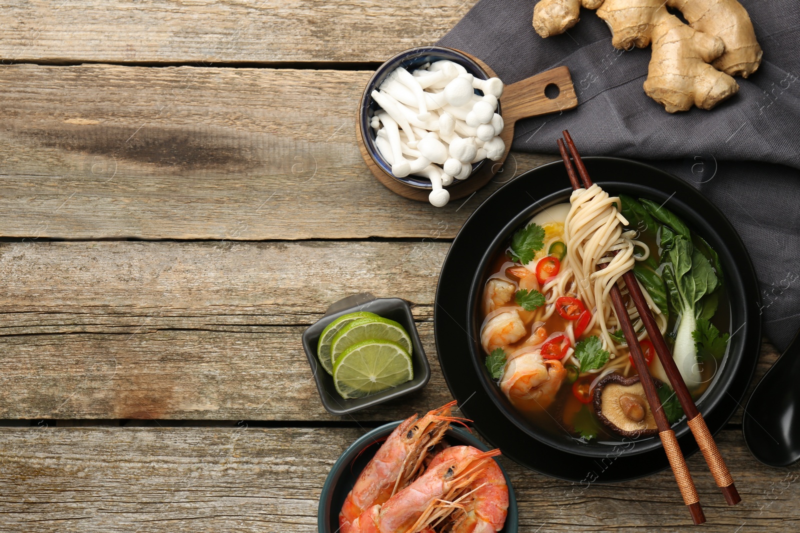 Photo of Flat lay composition with delicious ramen in bowl and ingredients on wooden table, space for text. Noodle soup