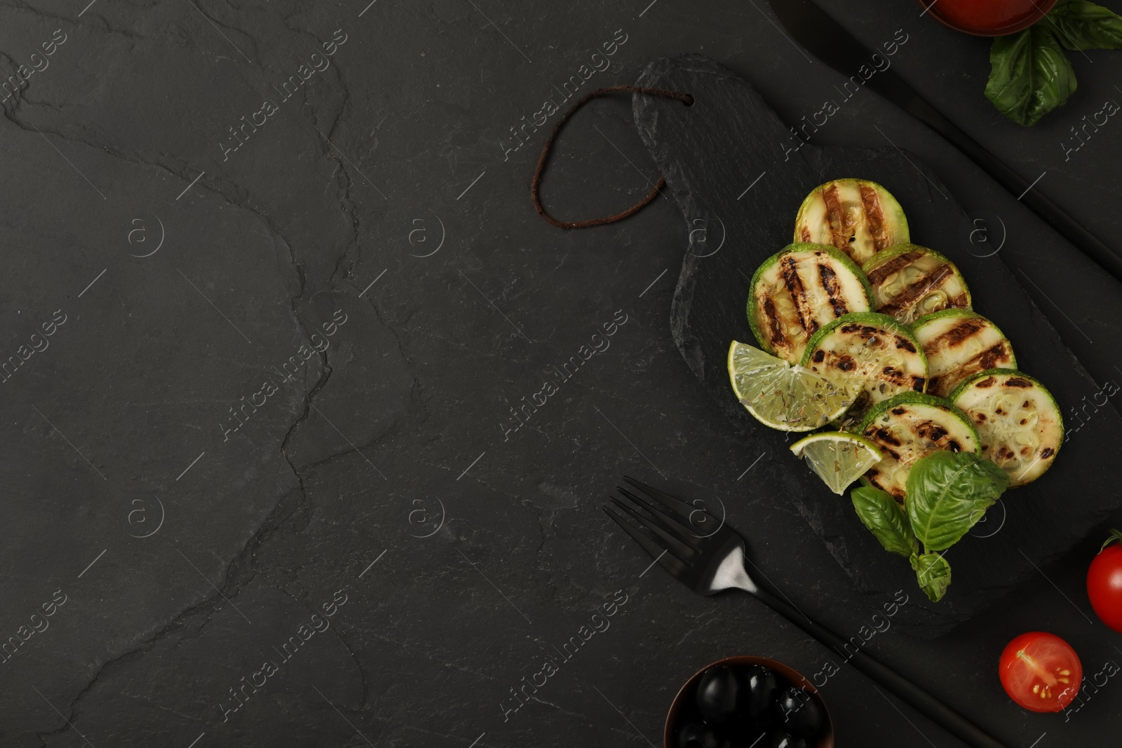 Photo of Delicious grilled zucchini slices served with lime and basil on black table, flat lay. Space for text