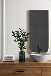 Photo of Eucalyptus branches and folded towels near stylish vessel sink on bathroom vanity. Interior design