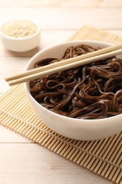 Photo of Tasty buckwheat noodles (soba) with chopsticks on wooden table, closeup