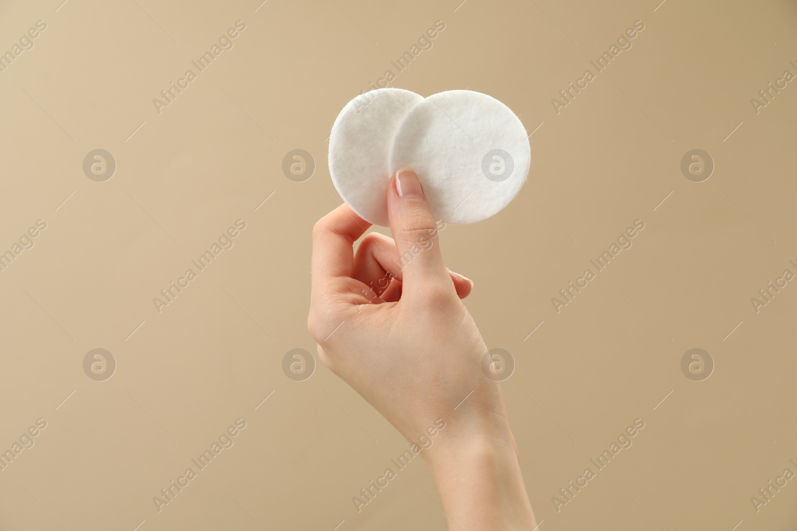 Photo of Woman holding cotton pads on beige background, closeup