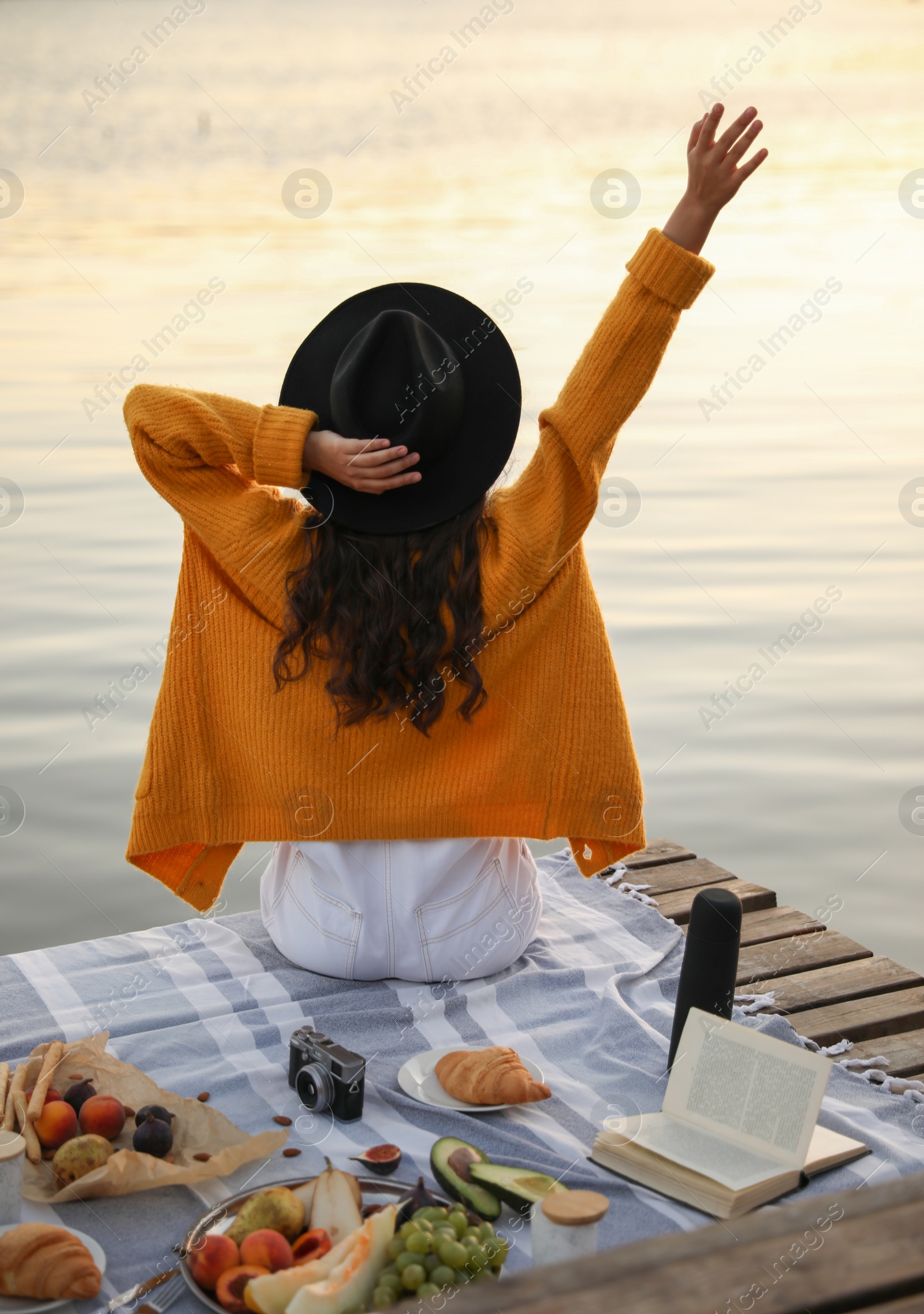 Photo of Young woman spending time on pier at picnic, back view