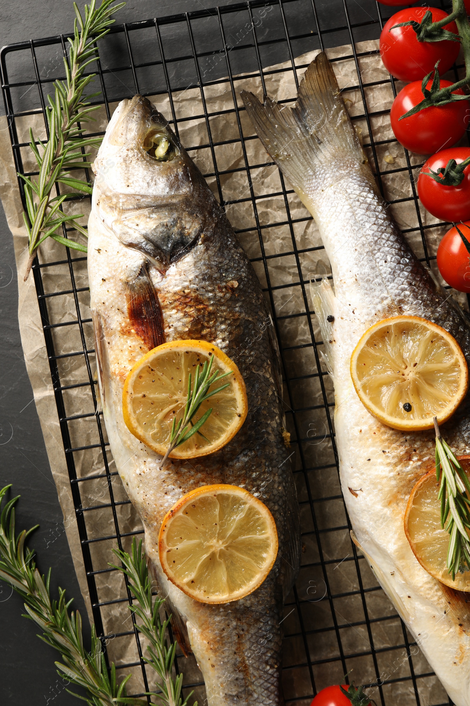 Photo of Baked fish with tomatoes, rosemary and lemon on black table, top view