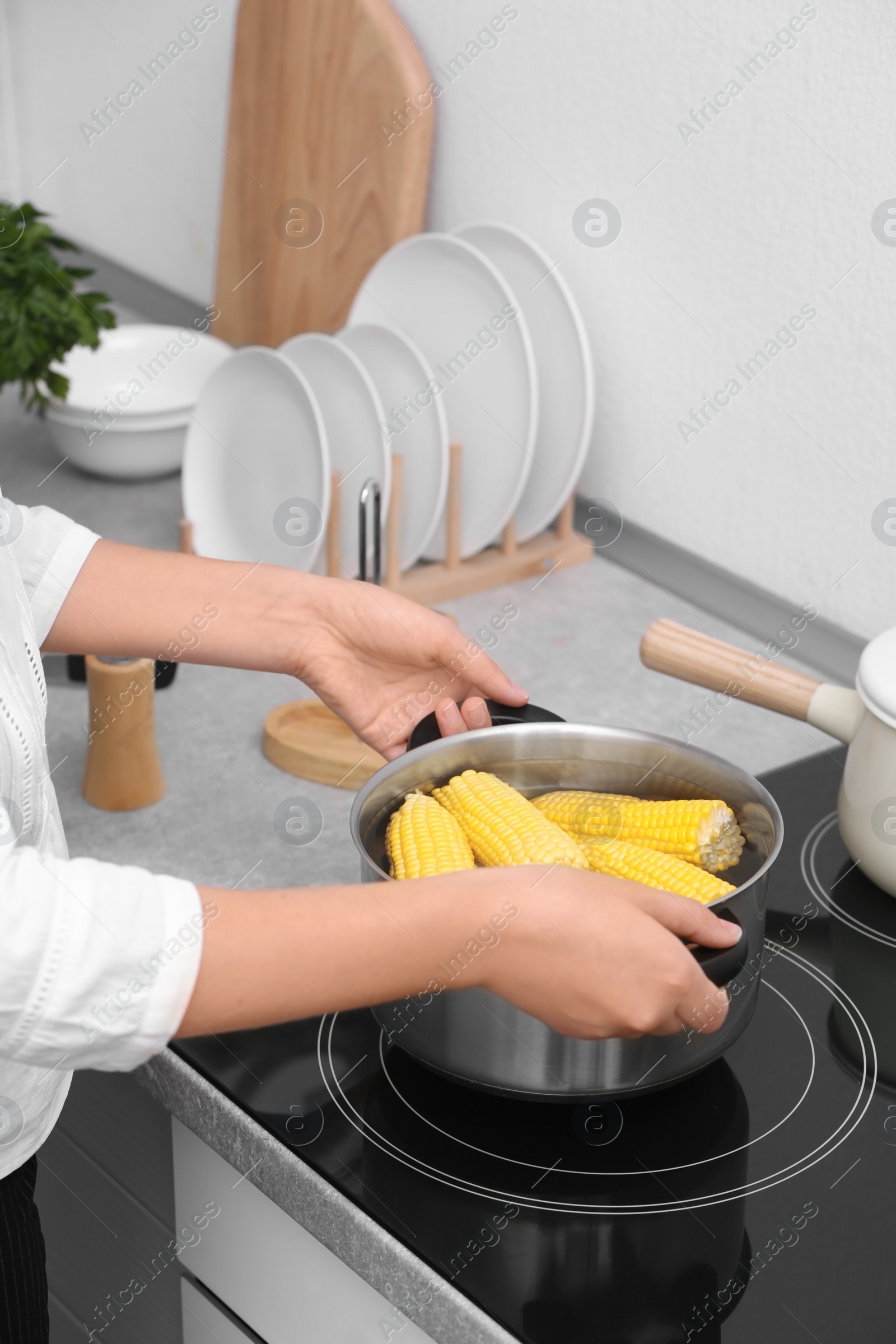 Photo of Woman preparing corn in stewpot on stove, closeup