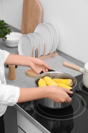 Woman preparing corn in stewpot on stove, closeup