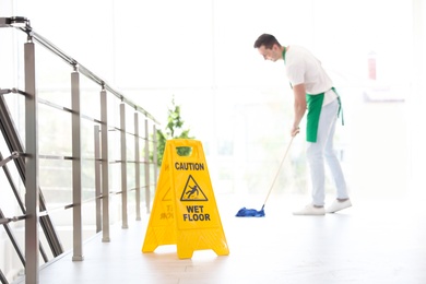 Safety sign with phrase "CAUTION WET FLOOR" and young man on background