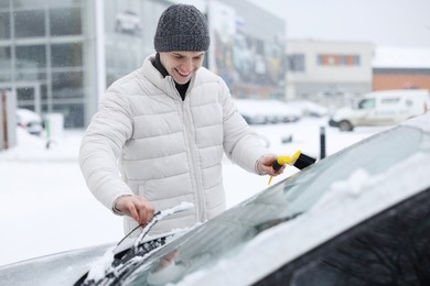 Photo of Man cleaning snow from car windshield outdoors