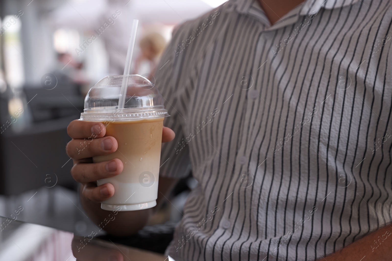 Photo of Man with plastic takeaway cup of delicious iced coffee in outdoor cafe, closeup