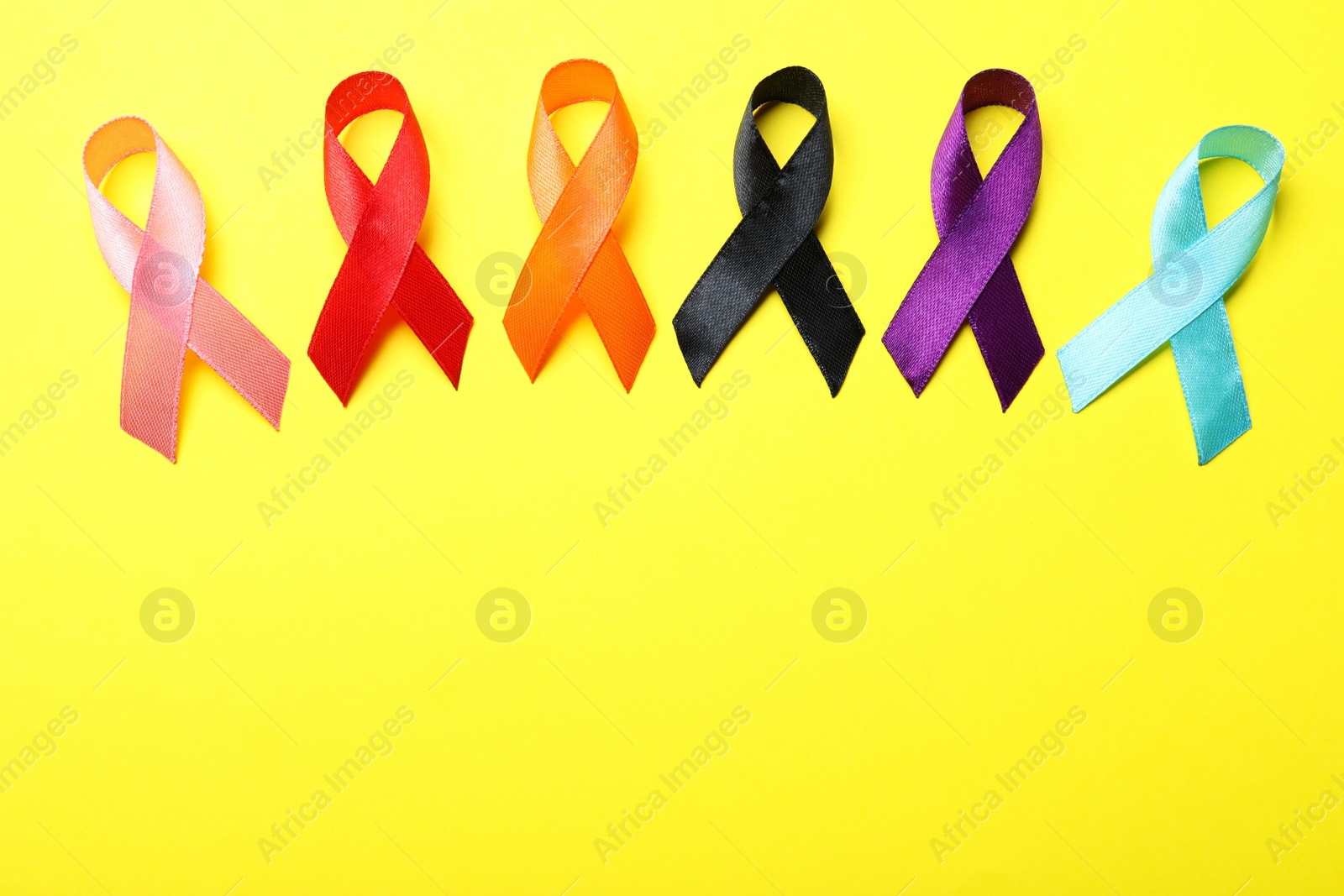 Photo of Colorful ribbons on yellow background, flat lay with space for text. World Cancer Day