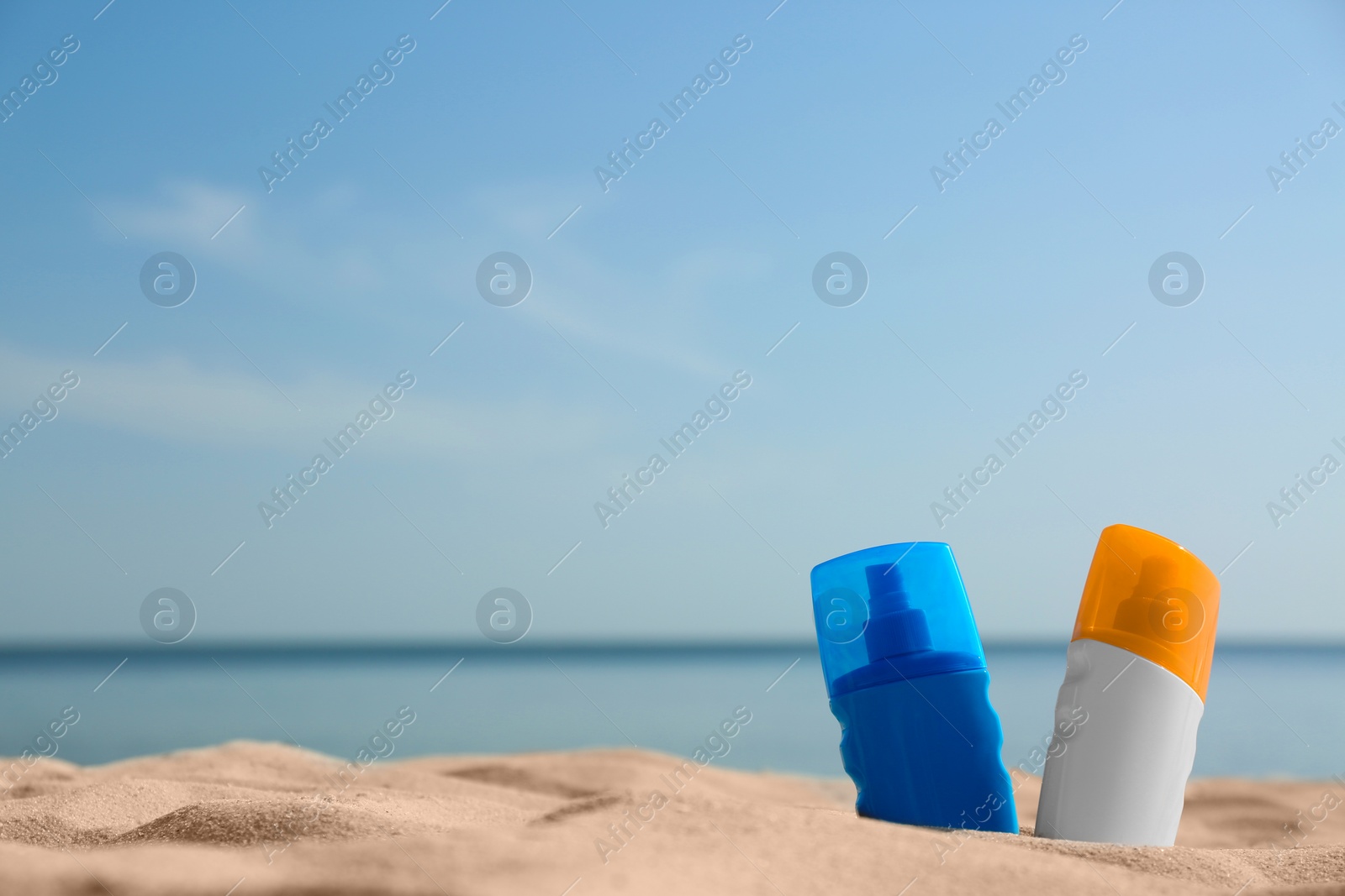 Photo of Bottles of sunblocks in beach sand near sea. Space for text