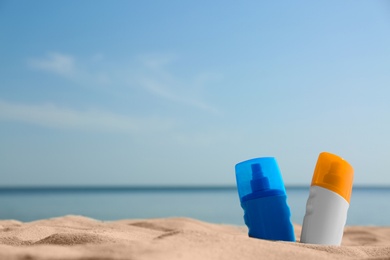 Photo of Bottles of sunblocks in beach sand near sea. Space for text