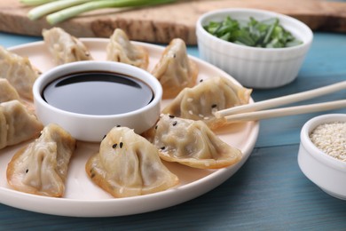 Delicious gyoza (asian dumplings), soy sauce and chopsticks on light blue wooden table, closeup