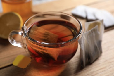 Photo of Tea bag in glass cup on wooden table, closeup