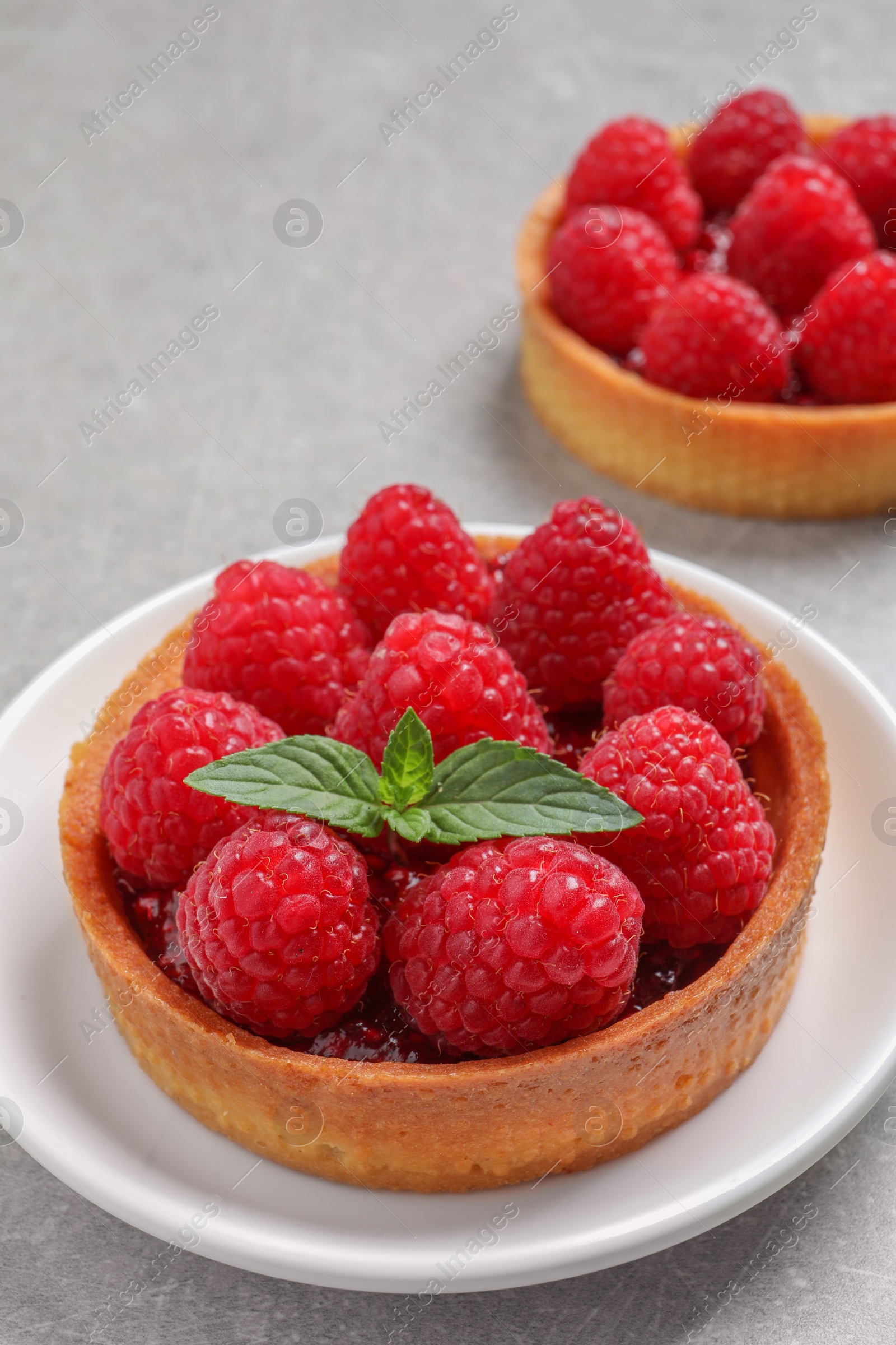 Photo of Tartlets with fresh raspberries and mint on light grey table. Delicious dessert
