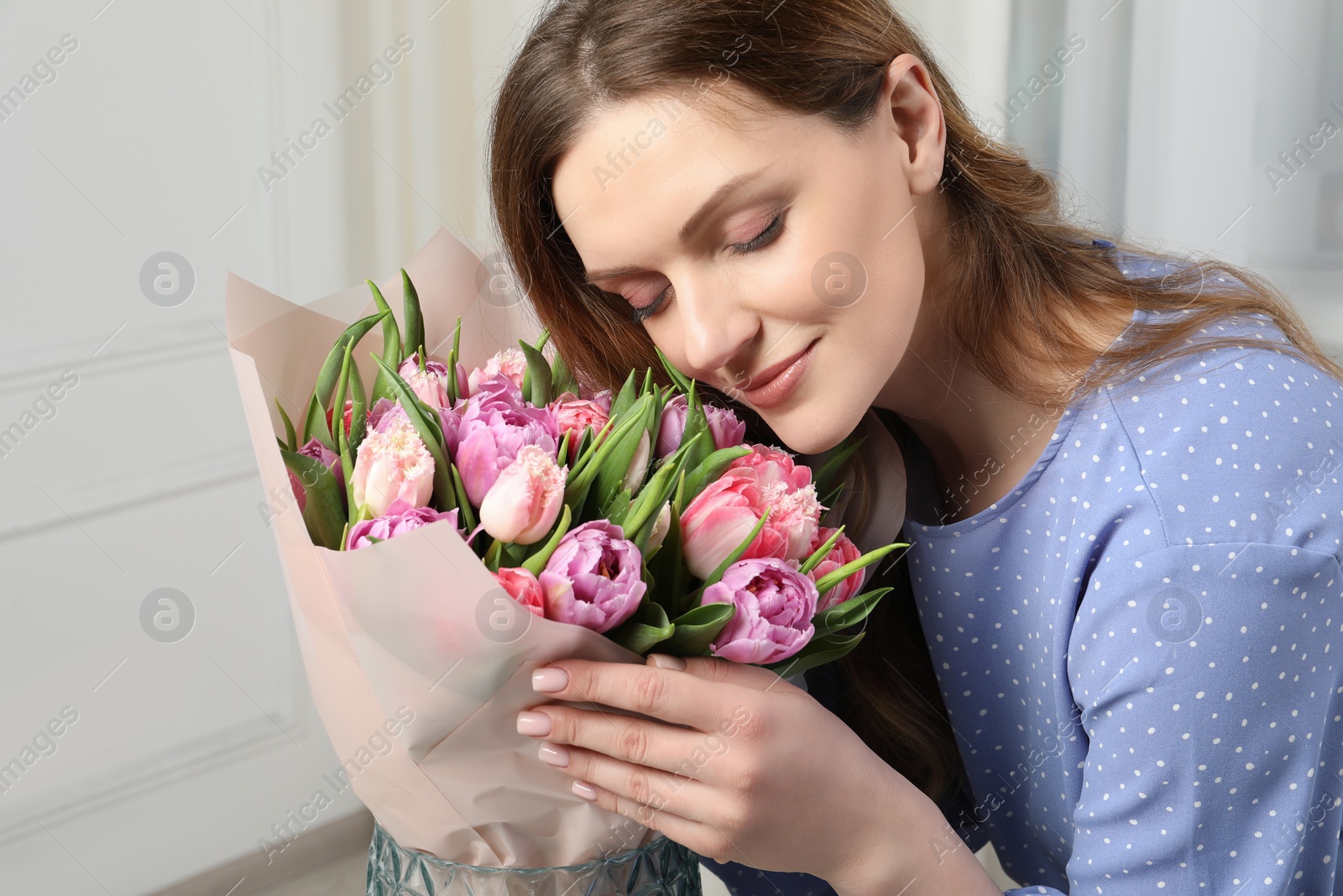 Photo of Young woman with bouquet of beautiful tulips indoors