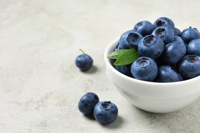 Bowl of fresh tasty blueberries on light grey table, closeup. Space for text