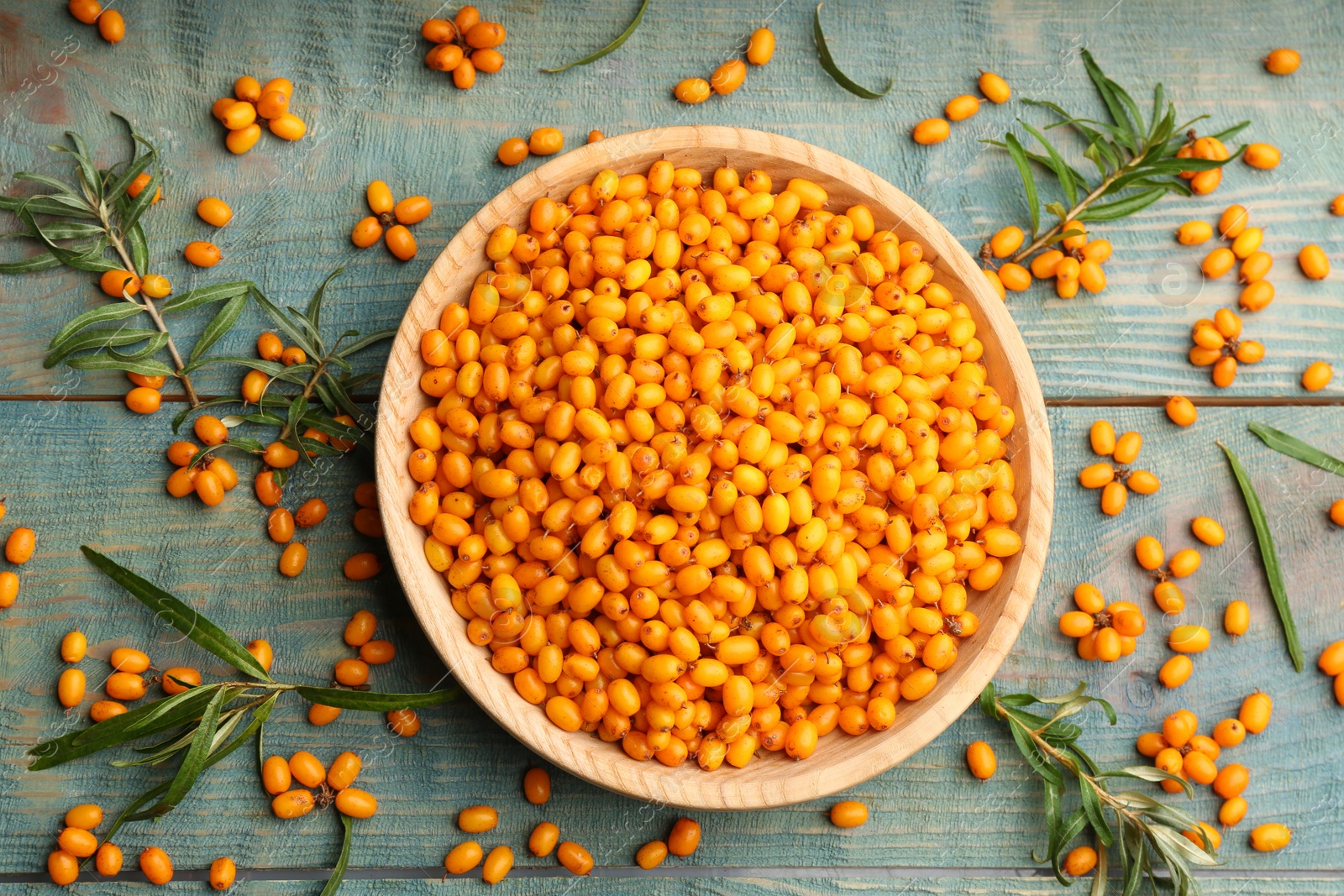 Photo of Ripe sea buckthorn berries on blue wooden table, flat lay