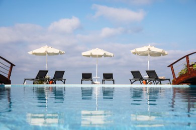 Photo of Chaise longues and beach parasols near outdoor swimming pool at resort