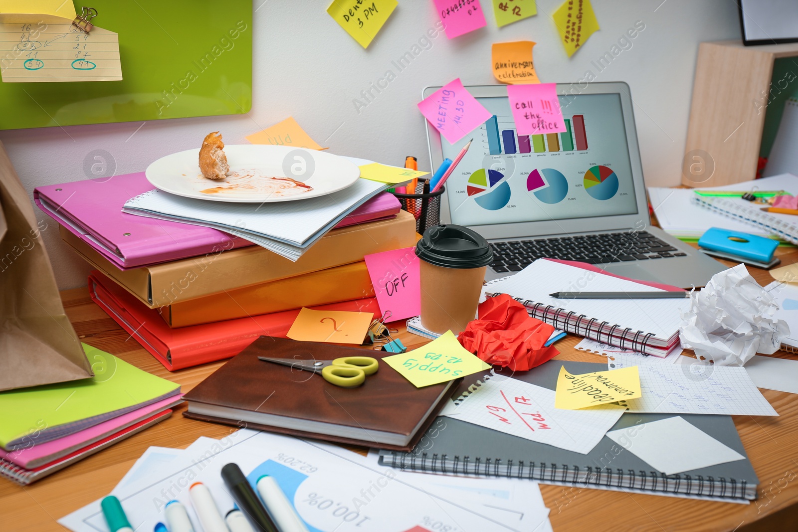 Photo of Messy table with laptop and stationery. Concept of being overwhelmed by work