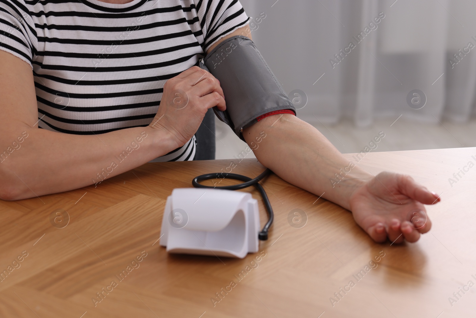 Photo of Woman measuring her blood pressure with tonometer at wooden table indoors, closeup