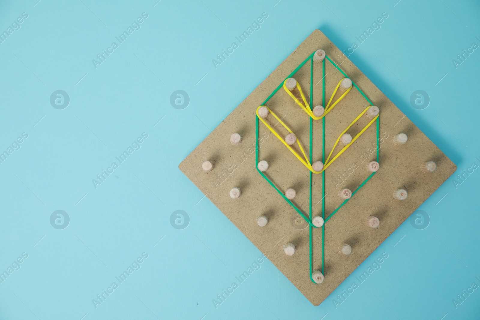 Photo of Wooden geoboard with leaf shape made of rubber bands on light blue background, top view and space for text. Educational toy for motor skills development