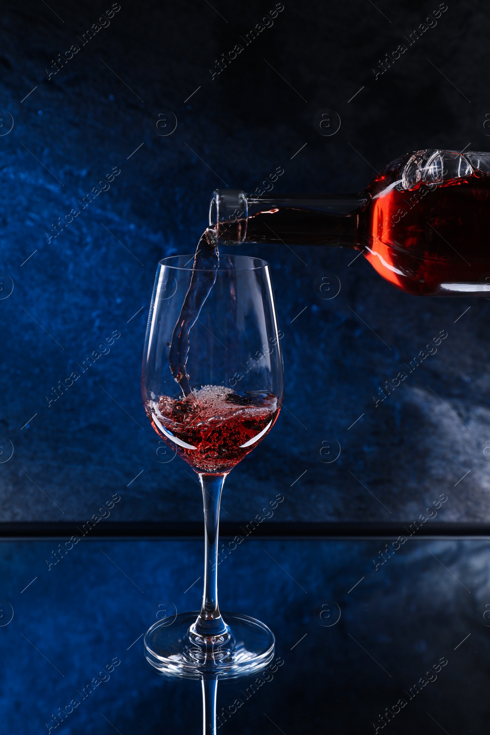 Photo of Pouring pink wine from bottle into glass on color background