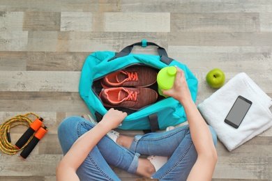 Photo of Young woman packing sports bag on floor, top view