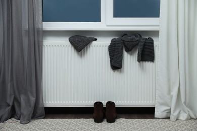 Heating radiator with hat, scarf and shoes near window indoors