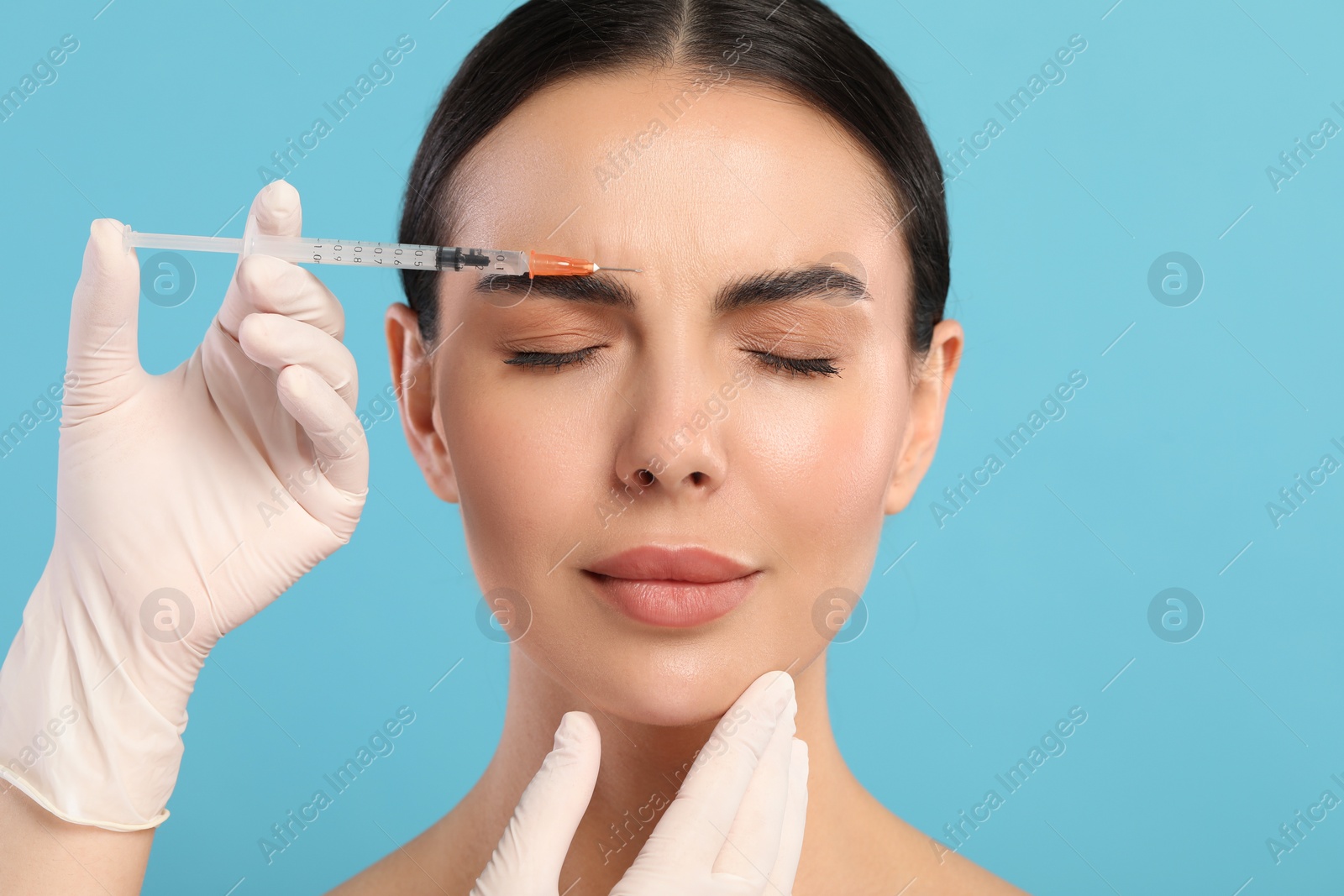 Photo of Doctor giving facial injection to young woman on light blue background. Cosmetic surgery